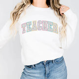 a woman wearing a white sweatshirt with the word teacher printed on it