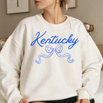 a woman sitting on a bed wearing a kentucky sweatshirt
