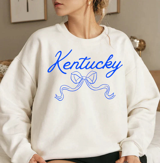 a woman sitting on a bed wearing a kentucky sweatshirt