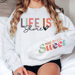 a woman sitting on top of a bed wearing a sweatshirt