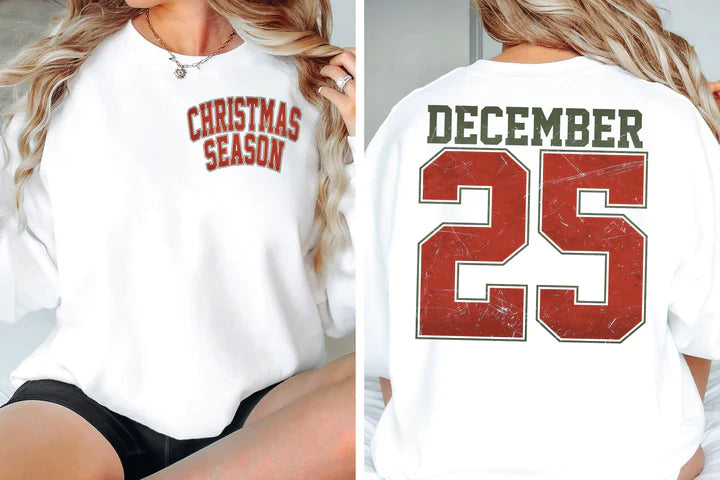 a woman sitting on a bed wearing a christmas sweatshirt