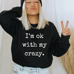 a woman wearing a black sweatshirt that says i'm ok with my crazy