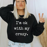 a woman wearing a black sweatshirt that says i'm ok with my crazy