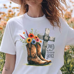 a woman standing in a field of flowers wearing a t - shirt with a cross