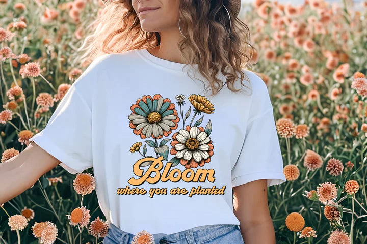 a woman standing in a field of flowers wearing a bloom t - shirt