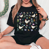a woman sitting on a bed wearing a black t - shirt with chickens on it