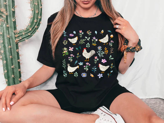 a woman sitting on a bed wearing a black t - shirt with chickens on it