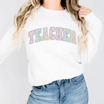 a woman wearing a white sweatshirt with the word teacher printed on it