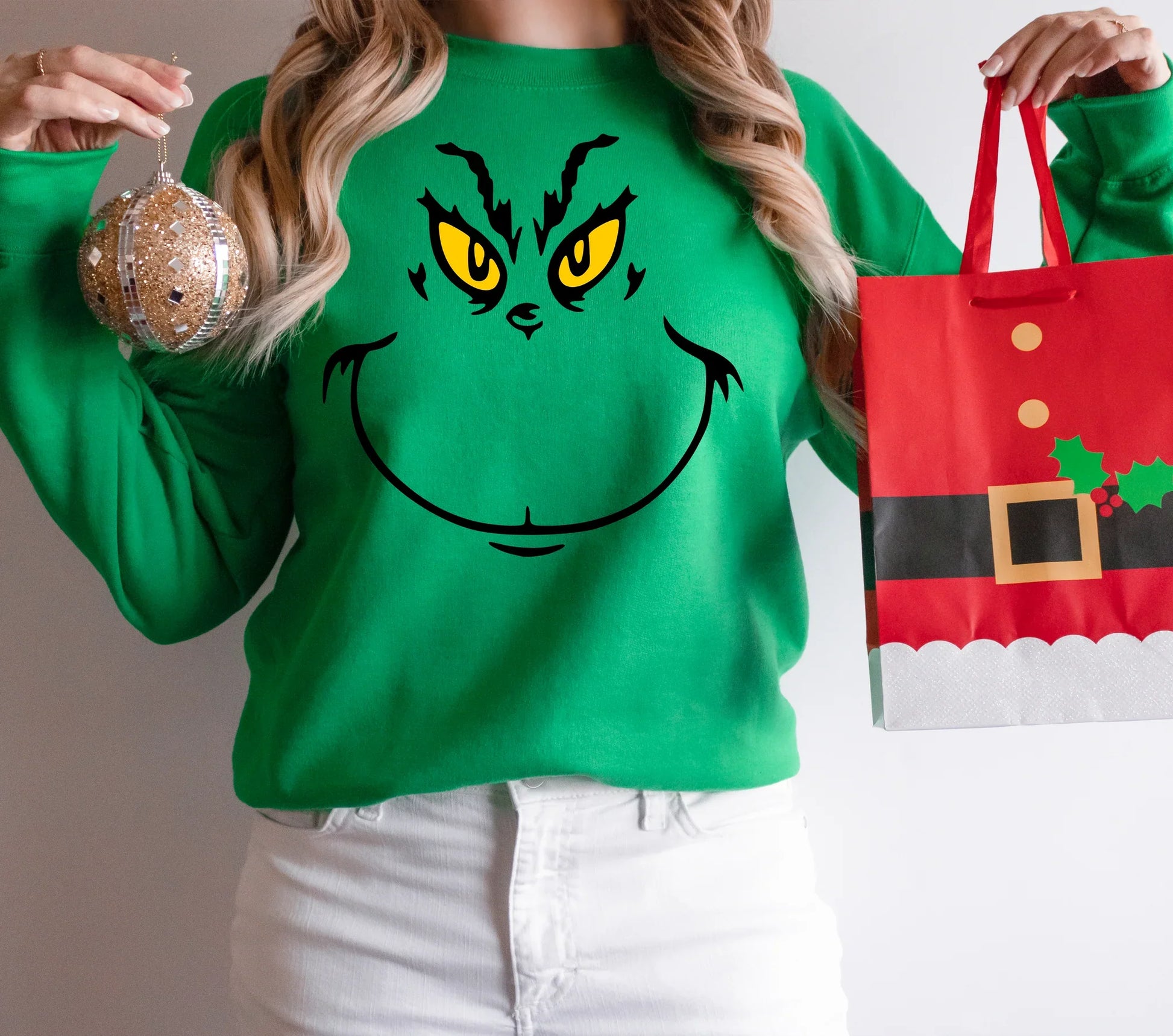a woman wearing a grin face sweater holding a christmas bag