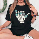 a woman sitting on a bed wearing a black t - shirt with a skeleton hand