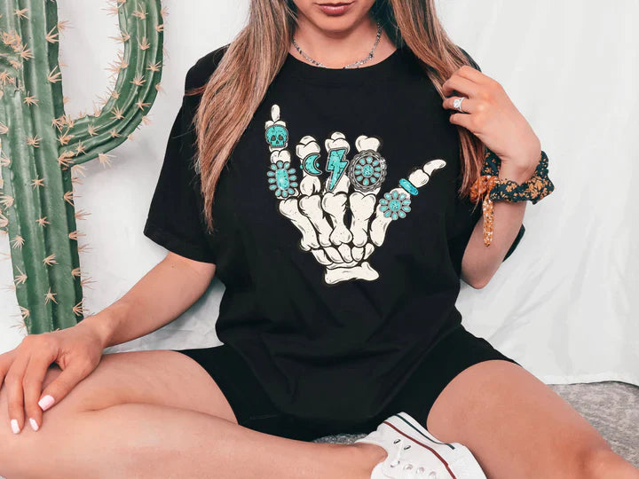 a woman sitting on a bed wearing a black t - shirt with a skeleton hand