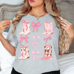 a woman standing in front of a bed wearing a gray shirt with pink bows and