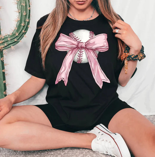 a woman sitting on the floor wearing a black shirt with a pink bow on it
